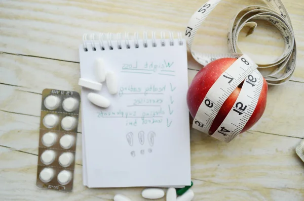 Measuring tape and apple with pills and note pad — Stock Photo, Image