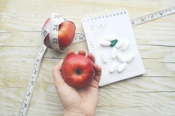 Mão feminina com fita métrica, comprimidos, maçãs e caderno — Fotografia de Stock