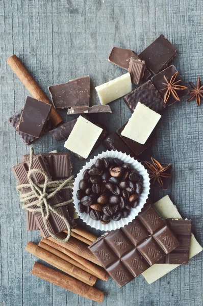 Bar of chocolate, coffee beans, hazelnuts, walnuts, cinnamon, coriander, spices .chocolate bar, candy bars,  different chocolate sweets on a wooden background.big choice of various sweets — Stock Photo, Image