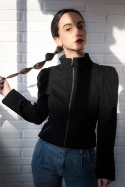 Kız örgüsünü tutarken gülümseyerek kameraya bakar.