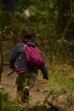 Okula geri dönüyor, çocuk sırt çantasıyla ormanda koşuyor.