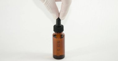 Eldivenli el beyaz arka planda ölçü şişesi olan bir damlatıcıyı alıyor.