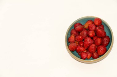 Beyaz arka planda izole edilmiş seramik kasenin içindeki taze çilekler.