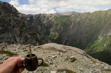 hand taking Argentine mate on top of the mountain, metal mate with light bulb,