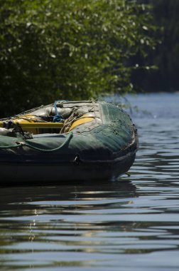 Sudaki kauçuk tekne, bitki örtüsü, insan yok ve kürek var.
