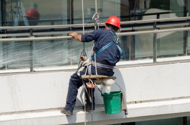 Miğferi ve iş kıyafetleri olan bir binada cam temizleme, iskele ile yükseklikte çalışma riski