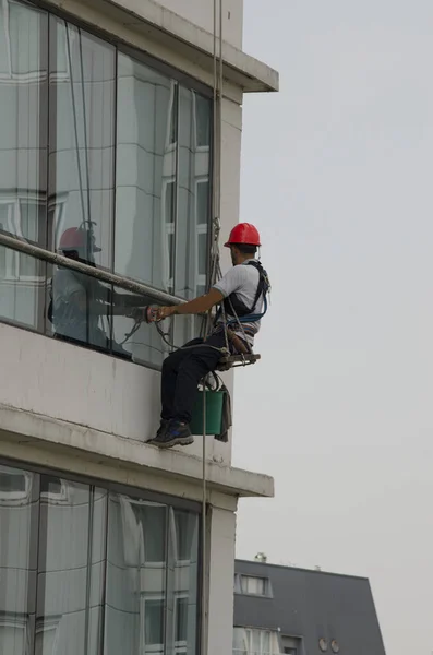 height glass cleaning, tall building glass cleaner with helmet and protective clothing. high-risk work with ropes and scaffolding