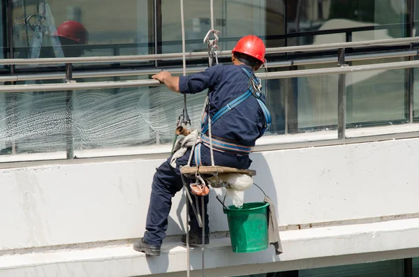 ヘルメットと作業着で建物内のガラスを清掃し足場で高さで作業する危険があります — ストック写真