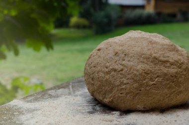 Ahşap tezgahın üzerinde kullanıma hazır buğday hamuru ve doğal gün batımı arka planı.