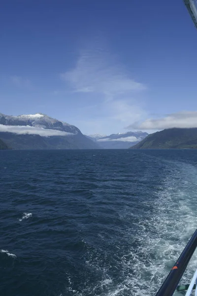 wake in the water, from the side of a boat in a lake with mountains and clouds. southern highway of chile