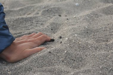 Erkek eli turkuaz ceketle kumsalda serin havayla dinleniyor.