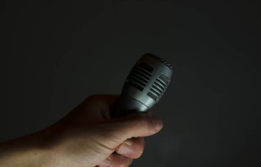 Gri arka planda el ele tutuşan gümüş mikrofon, şarkı söylemek, haber yapmak ya da kaydetmek anlamında
