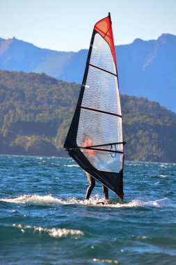 Mavi gölde rüzgar sörfü yapan bir kadın. Patagonya 'da arka planda dağlar. Arjantin.
