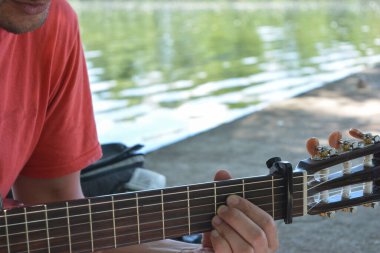 Gitar çalan genç bir adam, Creole ya da İspanyol gitarı, arka planda su var.