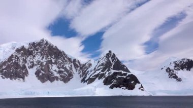 Kamera bu kayalık buzdağını soldan sağa doğru çeker. Beyaz bulutlar çizgili.