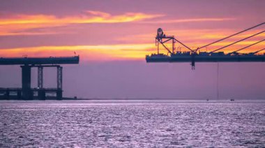 Vibrant twilight over the Tamkang Bridge construction in Tamsui New Taipei Taiwan. Workers welding on the bridge as sunset colors the sky orange and pink. Silhouette view.