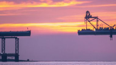 Vibrant yellow orange pink sunset over Tamkang Bridge silhouette with welding sparks falling into sea and boats at Tamsui Taiwan dusk.
