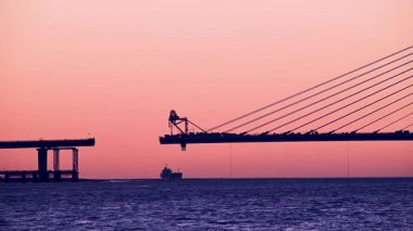 Vibrant twilight over the Tamkang Bridge construction in Tamsui New Taipei Taiwan. Workers welding on the bridge as sunset colors the sky orange and pink. Silhouette view.