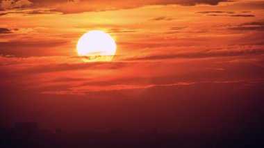 Intense close-up time-lapse of the sun sinking through thick clouds at sunset. The sky is a dramatic mix of fiery red and deep orange colors above New Taipei Taiwan.