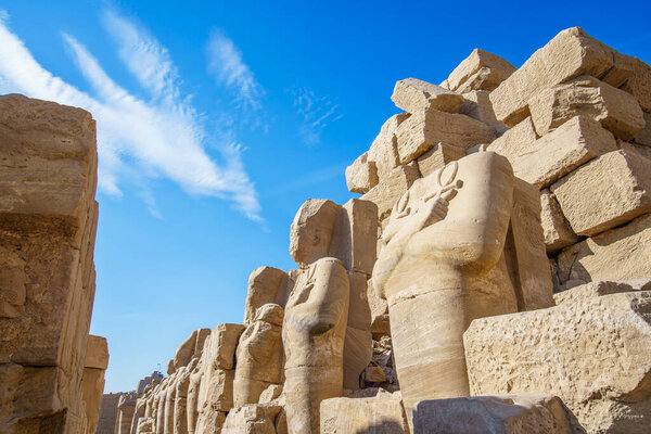 Обширные руины храма Карнак в Луксоре Египет с залитыми солнцем останками монументальных статуй и возвышающийся обелиск против ярко-голубого неба.