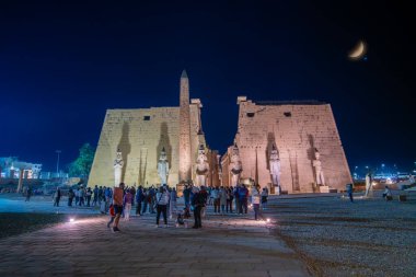 Luxor Tapınağı, Mısır - 18 Ocak 2025: Yüksek heykelleri ve yıldızlı gökyüzünün altında turistlerle dolu hilal şeklinde bir dikilitaşlı büyük antik tapınak.