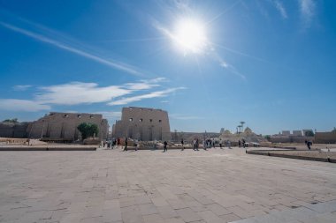 Luxor, Mısır - 18 Ocak 2025: Turistler parlak güneş altında Karnak Tapınağı kompleksinde geniş bir plazayı keşfettiler. Eski sütunlar ve harabeler avludan görülebiliyor..