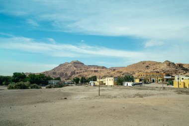 Luxor, Mısır - 18 Ocak 2025: Memnon Colossi yakınlarındaki kurak çöl manzarası, küçük binalar ve kayalık tepeler. Arkeolojik alanlar ve küçük köylerle karakterize edilir..