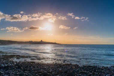 Shimen Bölgesi, New Taipei Şehri, Tayvan 'da yaz günbatımı sakin deniz, kayalık sahil ve uzak tepe siluetine yansıyan altın güneş ışığı.