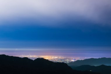 Jiangmayuan Sanyi Miaoli İlçesi Tayvan 'dan parlayan şehir ışıklarıyla dağların üzerinden akan bulutların muhteşem gece süreleri..
