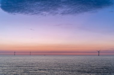 Tayvan 'ın Miaoli ilçesindeki Houlong Sahili' nde yaz günbatımının dingin güzelliğini yakalayın. Sakin denize, kayalık kıyılara ve renkli gökyüzünün altındaki uzak rüzgar türbinlerine hayranlık duy..