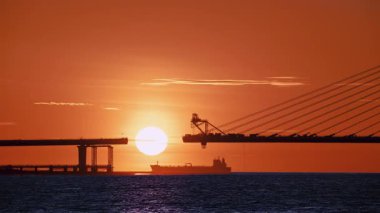 Canlı günbatımı siluetleri. Tamsui Yeni Taipei 'de inşa halindeki Danjiang Köprüsü' nde gemi ve parlayan ufuk çizgileri..