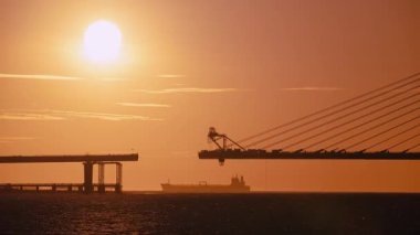 Bir feribot silueti dramatik günbatımı ile nehri geçiyor ve kablo, Tamsui New Taipei City Tayvan 'da Danjiang Köprüsü inşaatı devam ediyor.