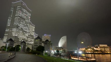 Sonbaharda Yokohama Minato Mirai 'nin gece manzarası. Rıhtım boyunca aydınlatılmış Cosmo Clock dönme dolabı ve modern gökdelenler..