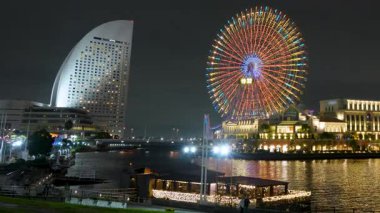 Yokohama, Japonya 'daki Minato Mirai' nin canlı sonbahar gecesi görüntüsü. Parlak ışıklandırılmış Cosmo saat dönme dolabı, modern gökdelenler, sakin deniz manzarası yansımaları ve parlayan şehir ışıkları..