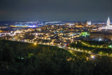 İspanya, Toledo 'nun göz kamaştırıcı şehri. Tarihi gökyüzü ve Rio Tajo nehri Mirador del Valle 'de karanlık bir gökyüzünün altında aydınlanır..