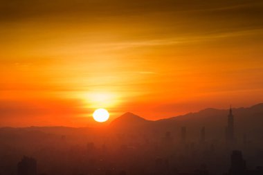 Tayvan 'daki Dadao Dağı' nda sonbahar şafağı erken başlıyor. Gün doğumuna tanık olun. Puslu bulutlarla örtülü turuncu bir gökyüzüne karşı dağ siluetleri olan rüya gibi bir manzara..