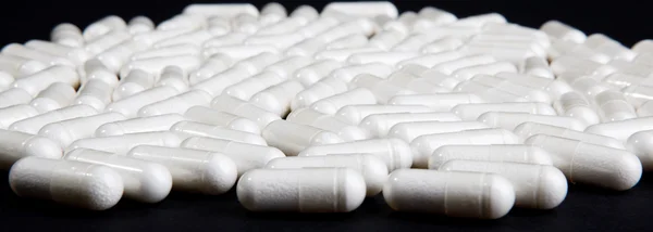 Pílulas brancas em preto — Fotografia de Stock
