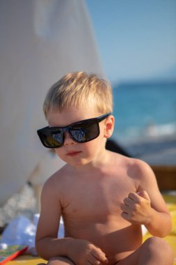 Sahilde güneş gözlüğü takan şık çocuk.