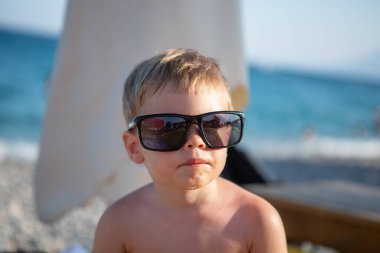 Sahilde güneş gözlüğü takan şık çocuk.