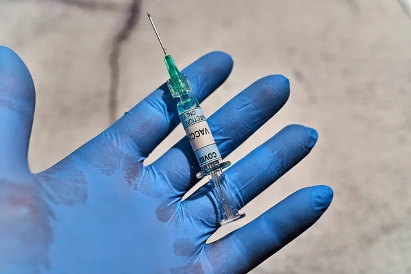 hand with a blue latex glove and one syringe in vertical position that has written \
