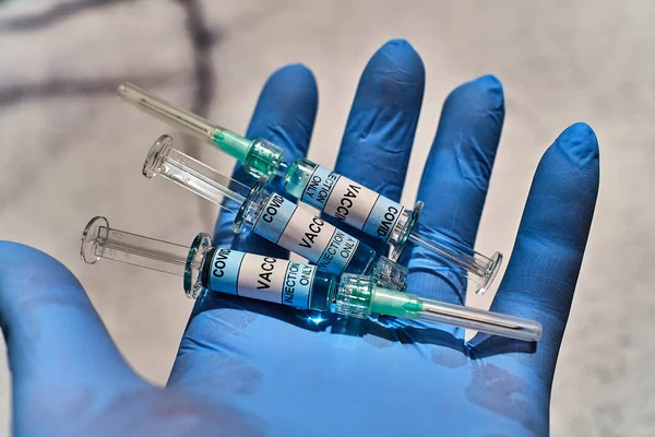 ラベルに Covid 19ワクチンのみ注射 と書かれた青いラテックス手袋と水平位置の3本の注射器を手に — ストック写真