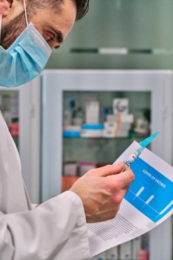 Yüz maskesi takan genç beyaz adam, rapor simülasyonu ve aşısı olan tıbbi elbise.