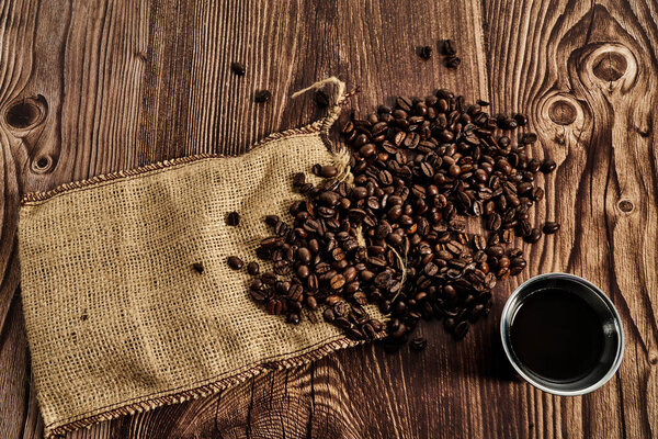 hand holding cup of black coffee over coffee beans on a wooden table