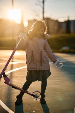 Paltolu kız portresi ve gün batımında pembe scooter.