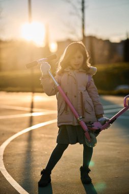 Paltolu kız portresi ve gün batımında pembe scooter.