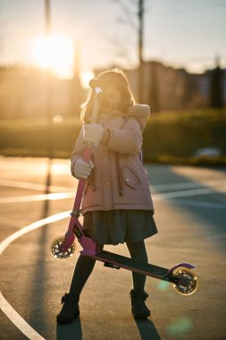 Paltolu kız portresi ve gün batımında pembe scooter.