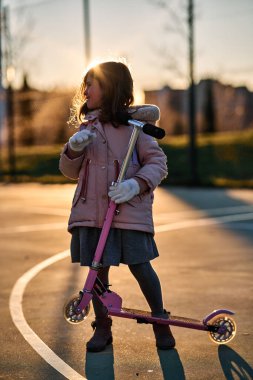 Paltolu kız portresi ve gün batımında pembe scooter.