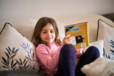 Kanepede oturup kitap okuyan küçük bir kız..