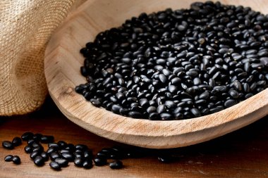 Siyah bir arka planda, tahta kaşıkta siyah fasulyeler.