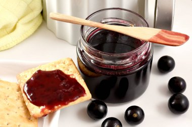 Brezilya üzümleri jaboticaba meyvesi, jöle kavanozunda beyaz bir kavanoz, bardak, tost, spatula, üzümler, beyaz bir tahta üzerinde sarı bez ve beyaz bir arka plan.